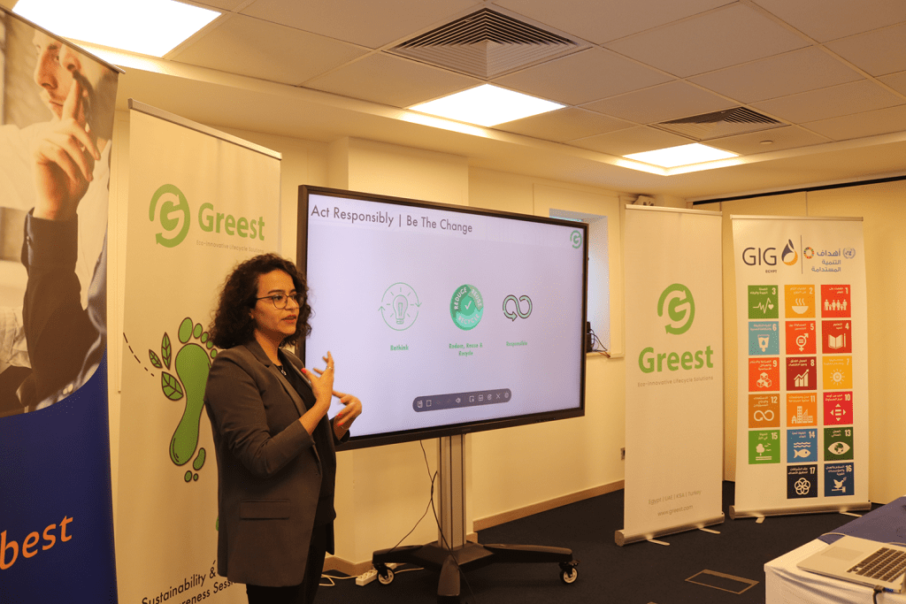 A presenter stands beside a large screen displaying sustainability principles: "Rethink, Reduce, Reuse & Recycle, and Responsible."